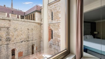 A hotel room with a large window overlooking a historic stone building with arches and a tower.