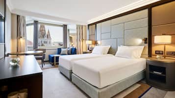 Quarto de hotel com duas camas, uma escrivaninha, uma cadeira, uma mesinha e vista para um edifício.