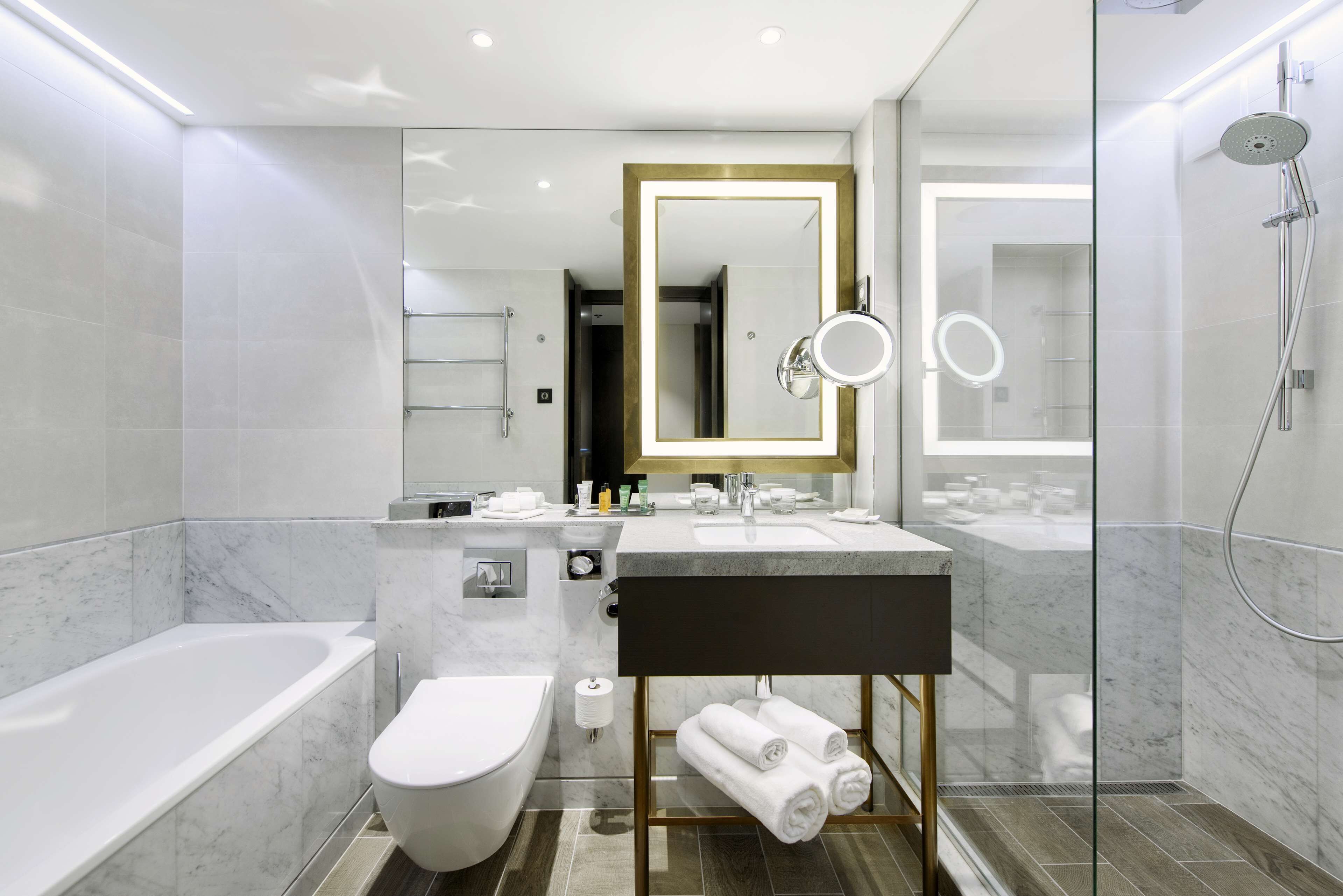 A modern bathroom with a bathtub, toilet, and dual sinks with a large mirror.