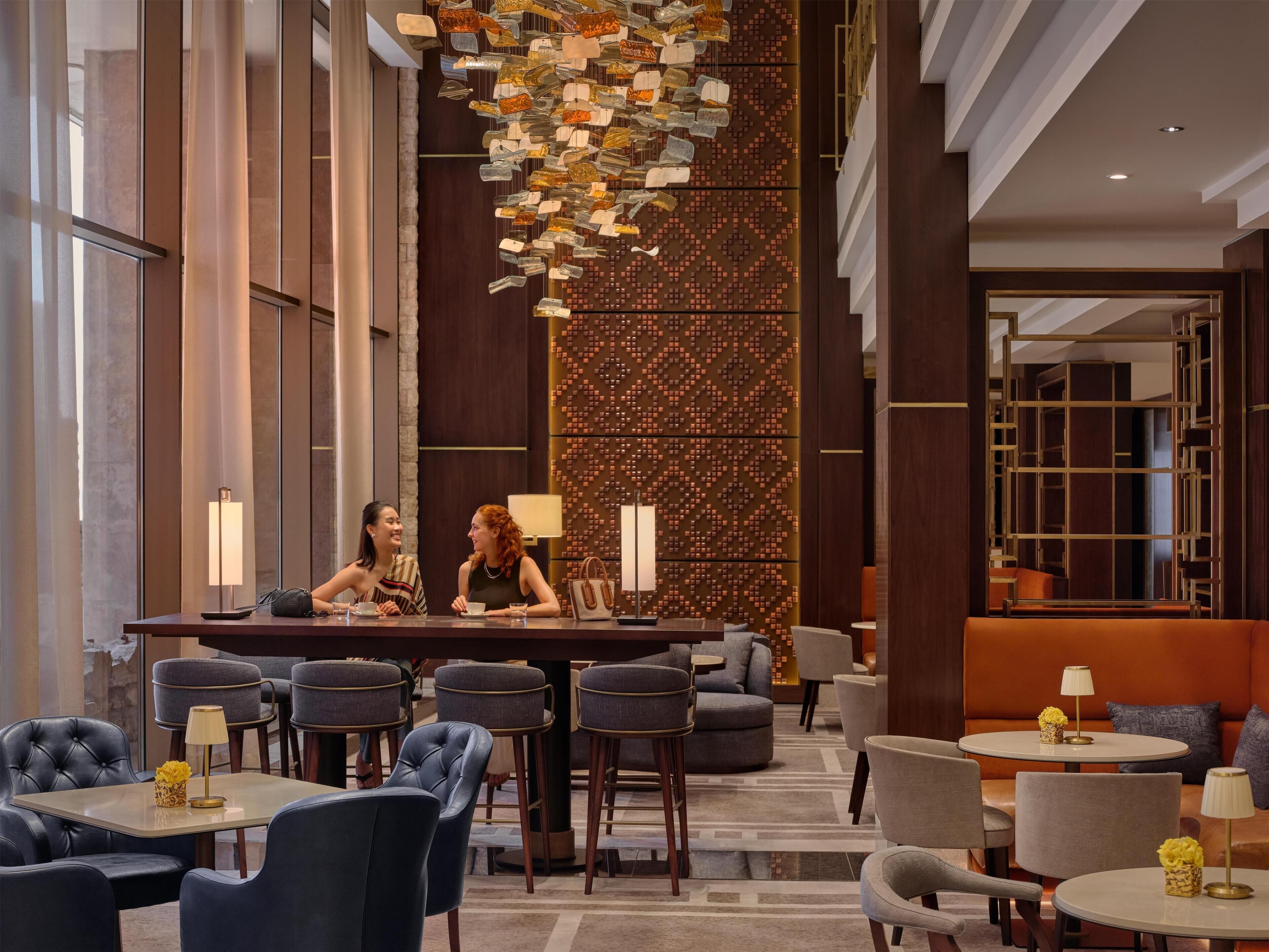 A modern hotel lobby with a bar area, seating arrangements, and a decorative wall.