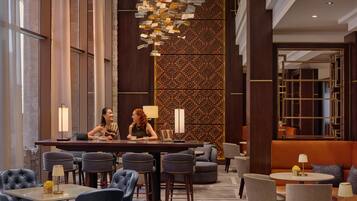 En moderne hotellobby med barområde, siddepladser og en dekorativ væg.