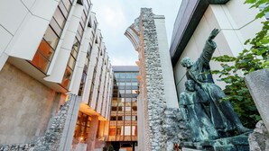 A modern building with a stone facade, a glass entrance, and a statue of a historical figure. - Hilton Budapest (Budapest)