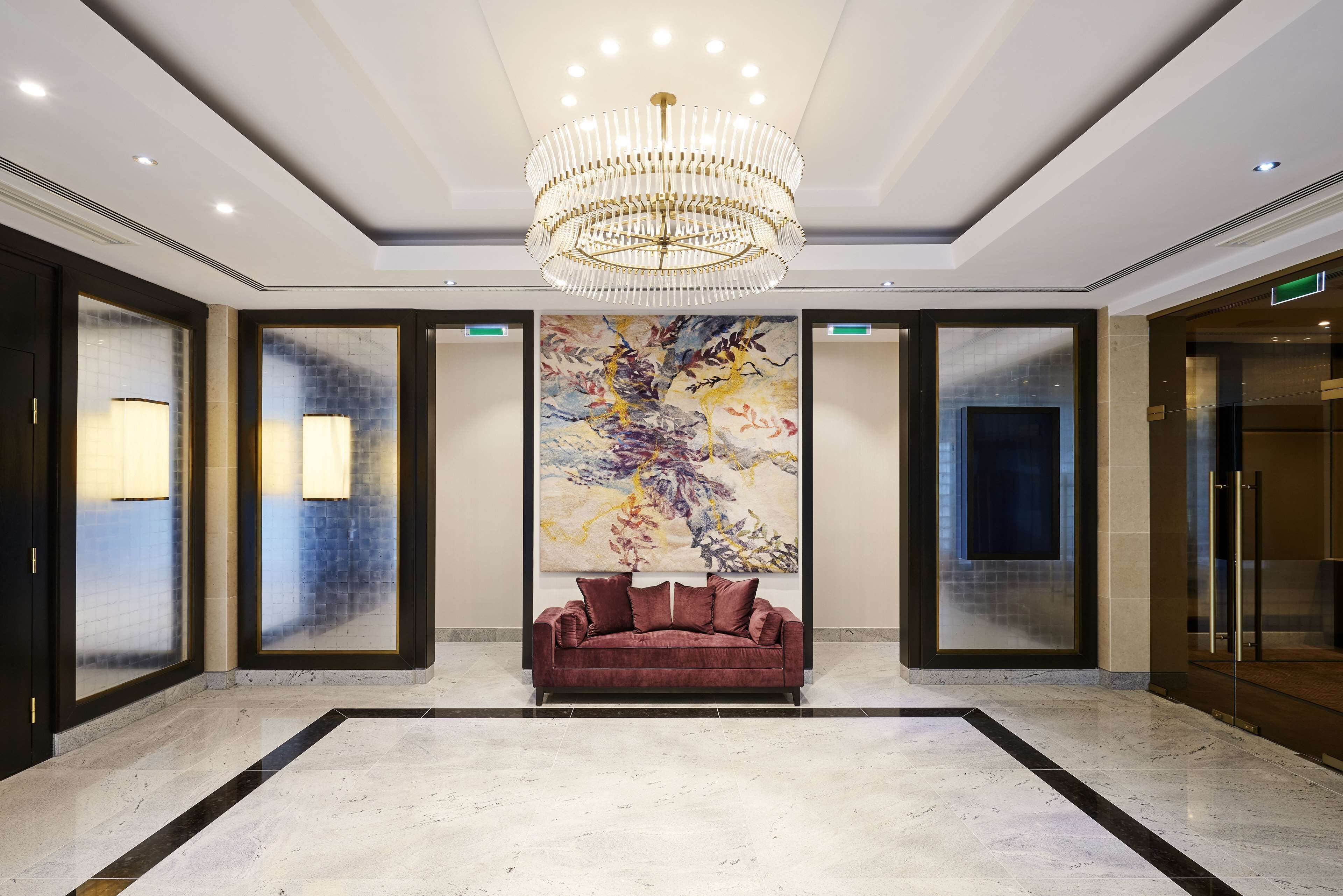 A lobby with a red sofa, a chandelier, and a large abstract painting on the wall.
