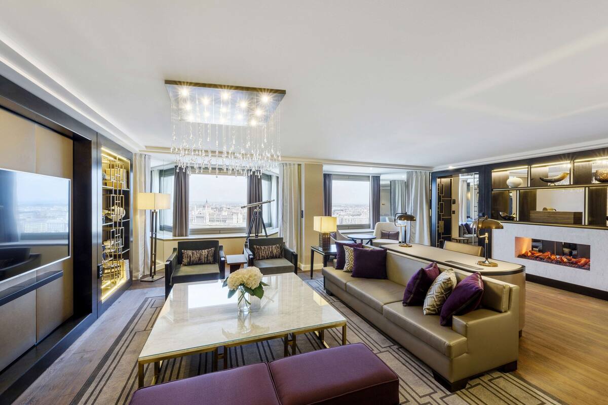 Une chambre d’hôtel moderne dotée d’une grande fenêtre, d’un lustre, d’un canapé, d’une table à manger et d’un téléviseur.