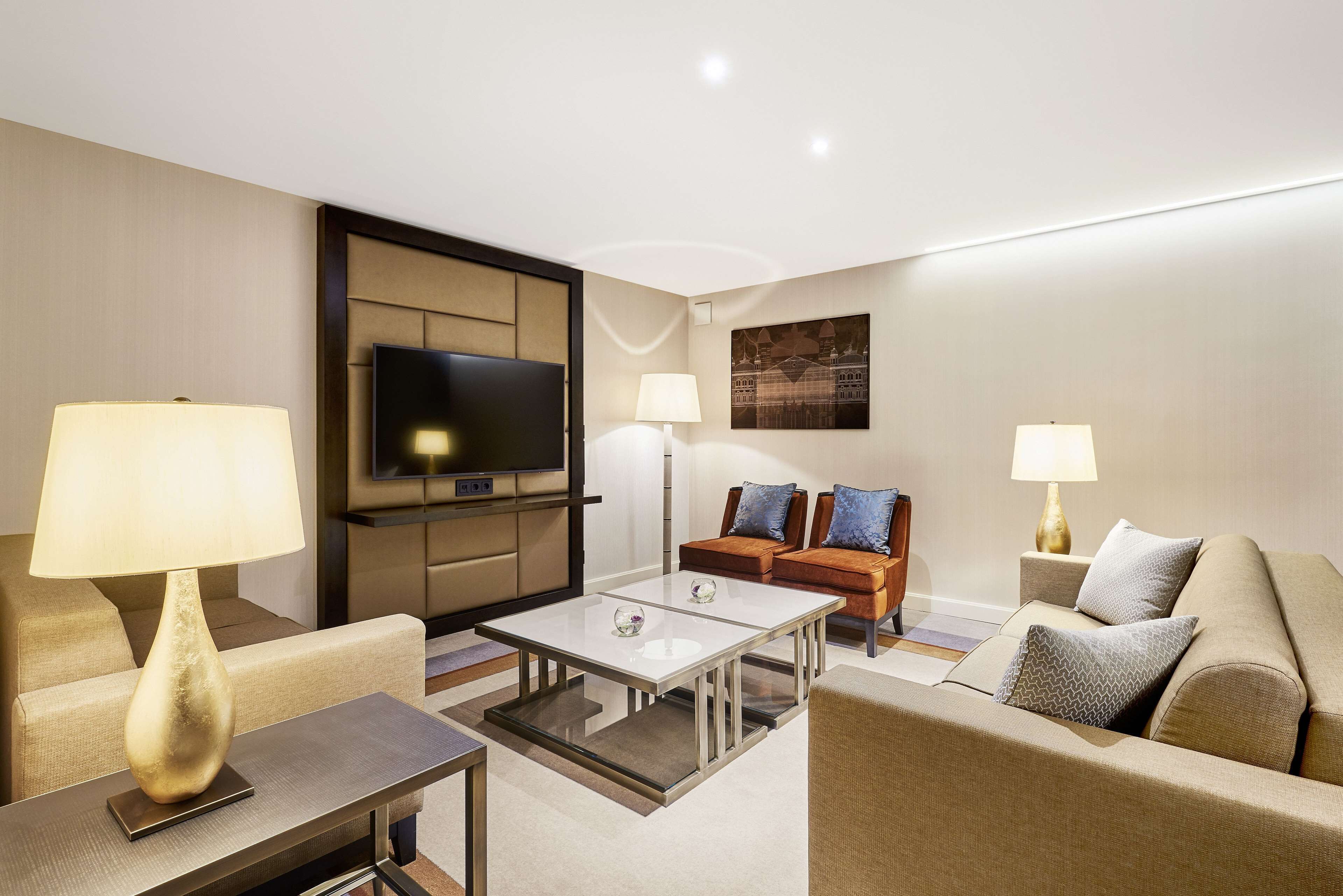 A modern hotel room with a flat-screen TV, two sofas, a coffee table, and two lamps.
