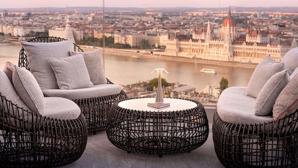 A balcony with wicker furniture and a view of a cityscape including a prominent building. - Hilton Budapest (Budapest)