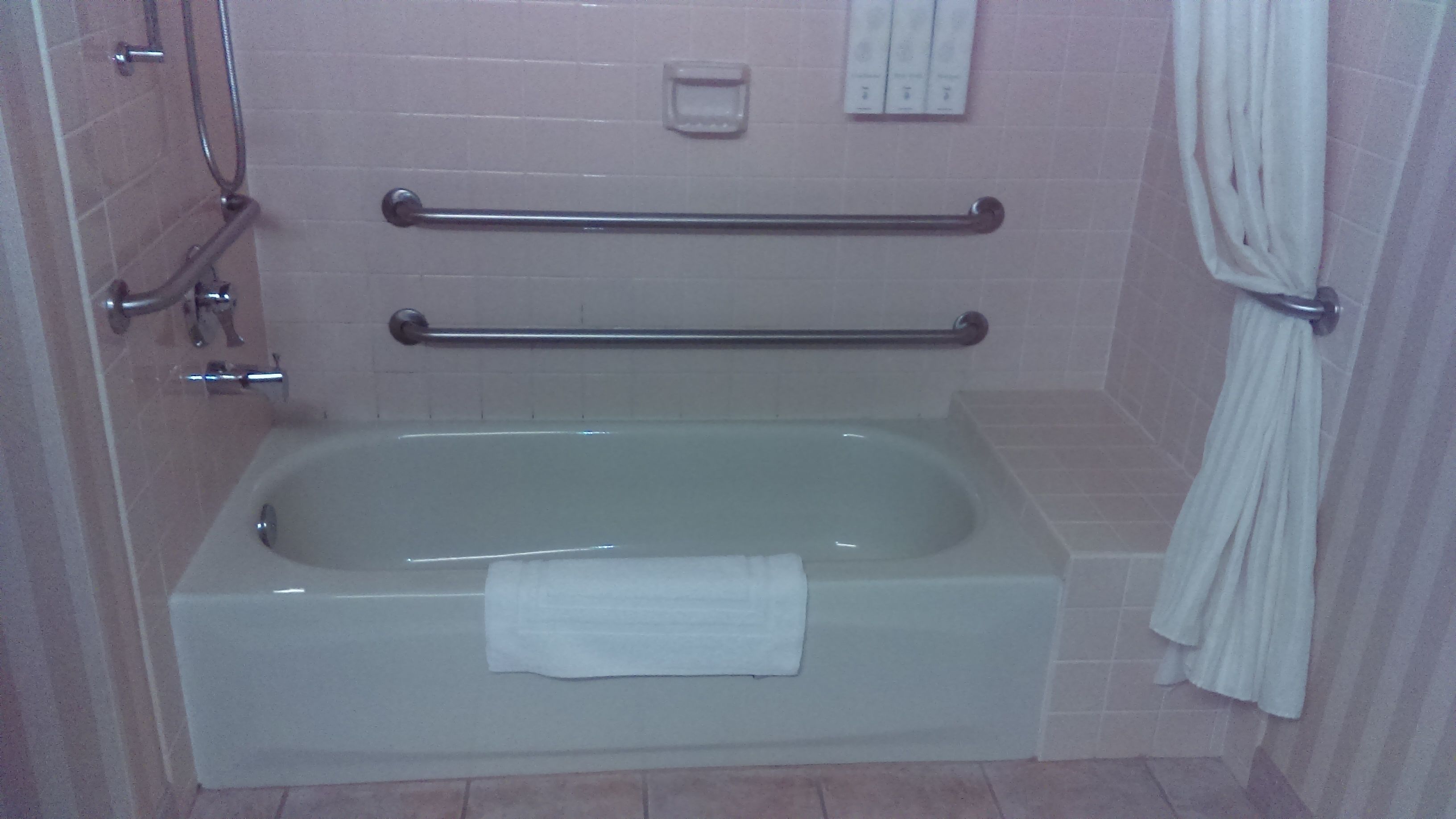 A bathroom with a bathtub, grab bars, a towel rack, and a shower area.