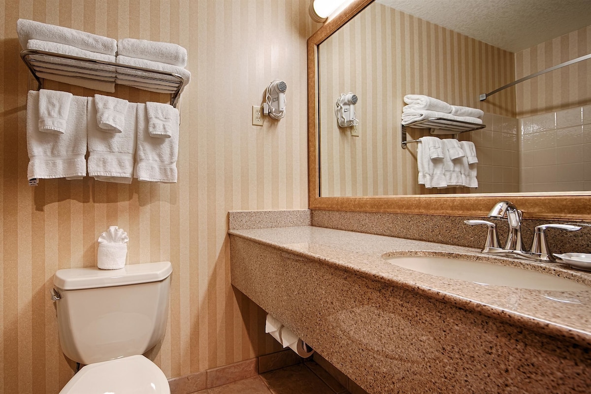 Une salle de bain comprenant des toilettes, un lavabo avec un plan de travail en granit et un porte-serviettes avec des serviettes pliées.