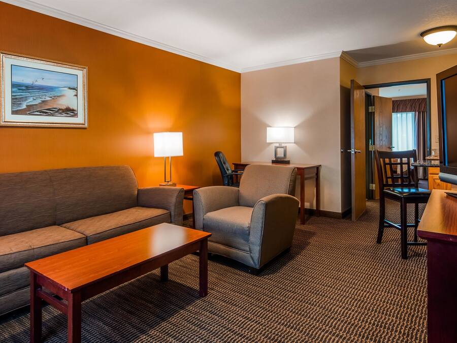 A hotel room with a sofa, armchair, small table, lamp, TV, and a painting on the wall.