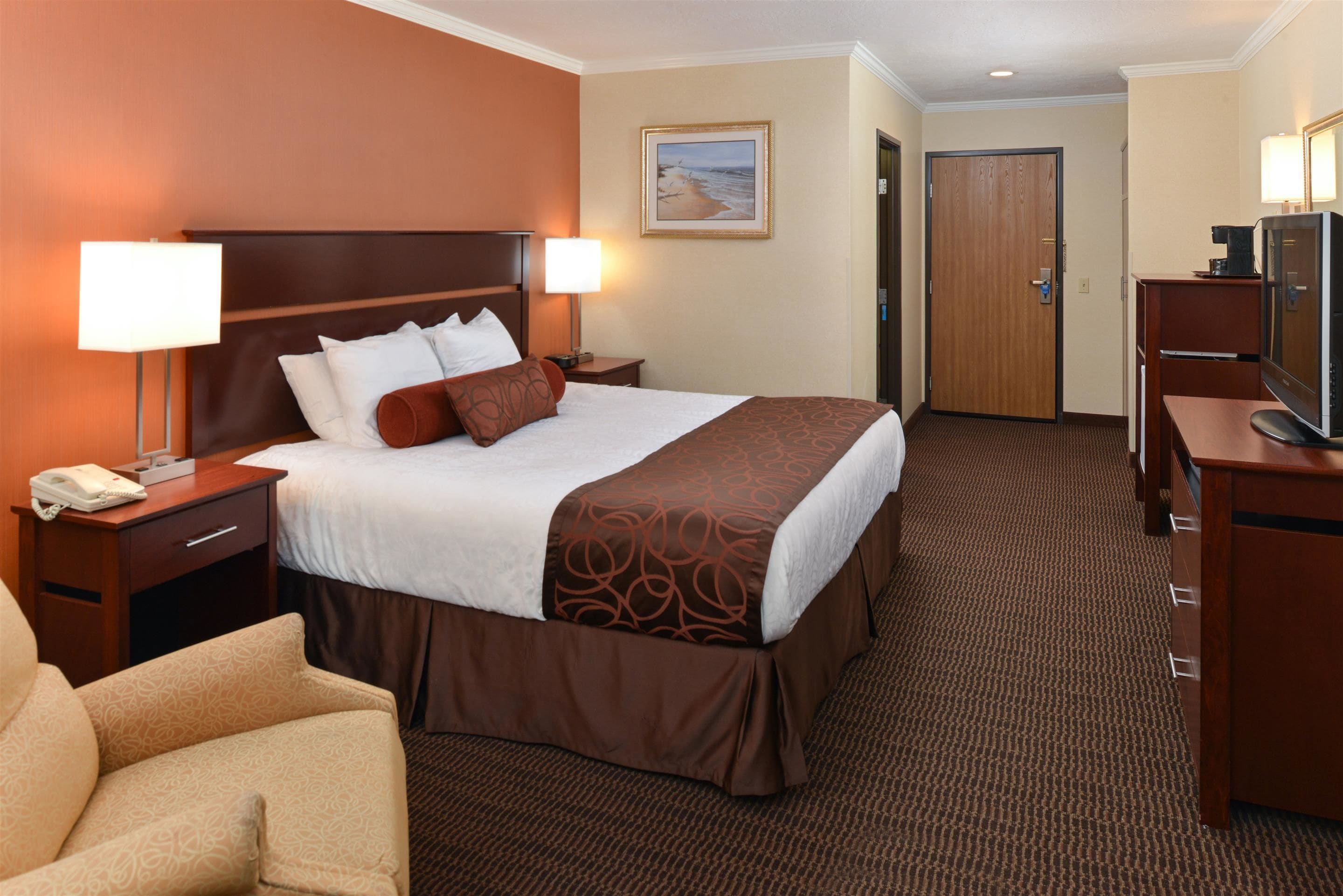 A hotel room with a large bed, two bedside tables with lamps, a desk with a television, and a door leading to another room.