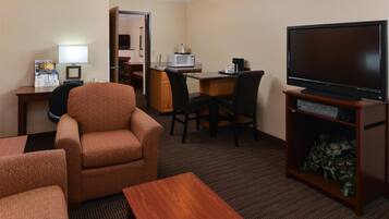 A hotel room with a TV, a desk with a microwave, a chair, a sofa, and a small table.