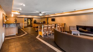 Un hall d’hôtel avec un comptoir d’accueil, un espace repas avec des chaises en bois, un canapé et un ventilateur de plafond.