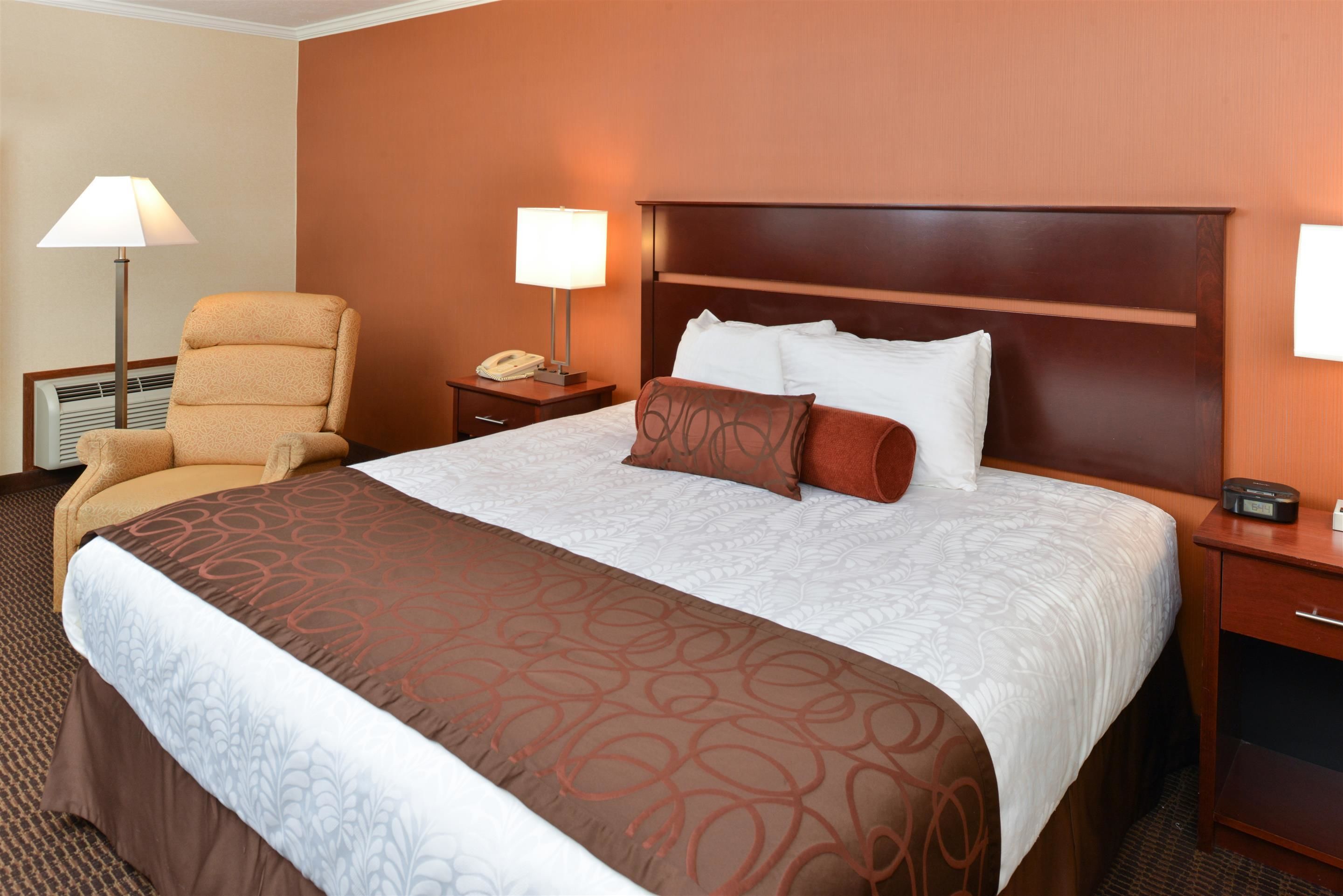 A hotel room with a large bed, a chair, a nightstand with a lamp, and a telephone.