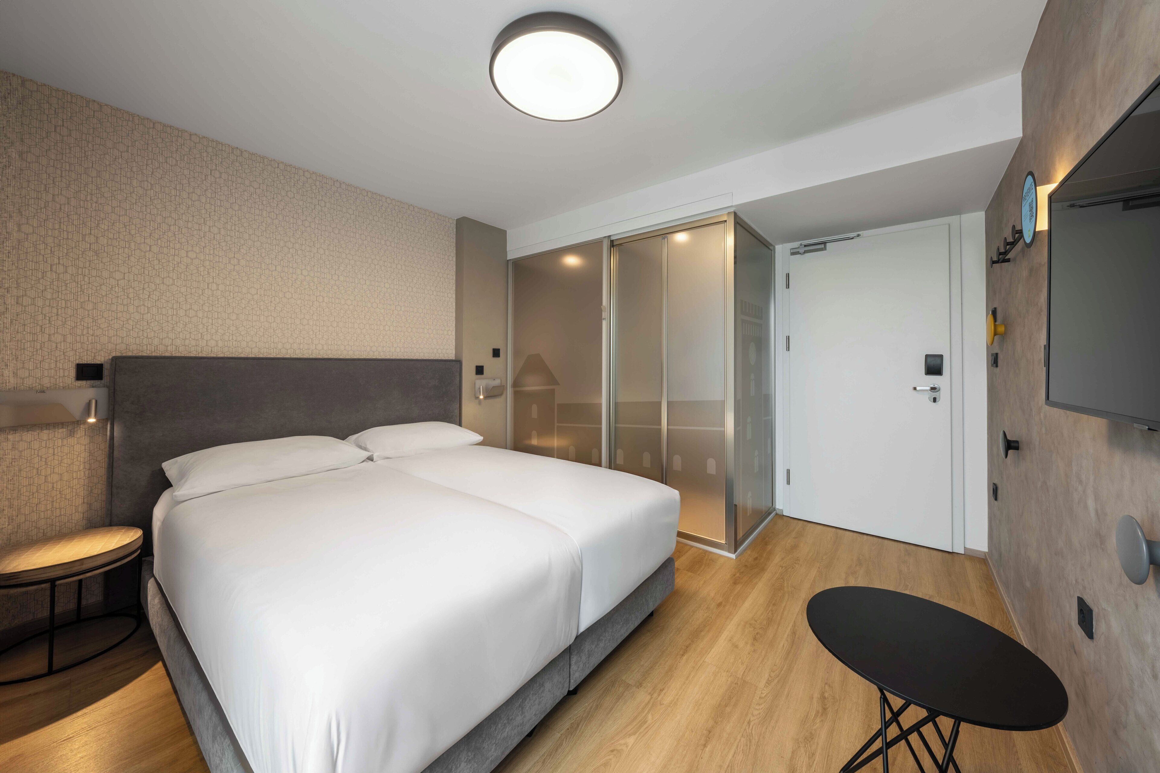Une chambre d’hôtel moderne avec un grand lit, une petite table ronde, un téléviseur et un placard à portes coulissantes.
