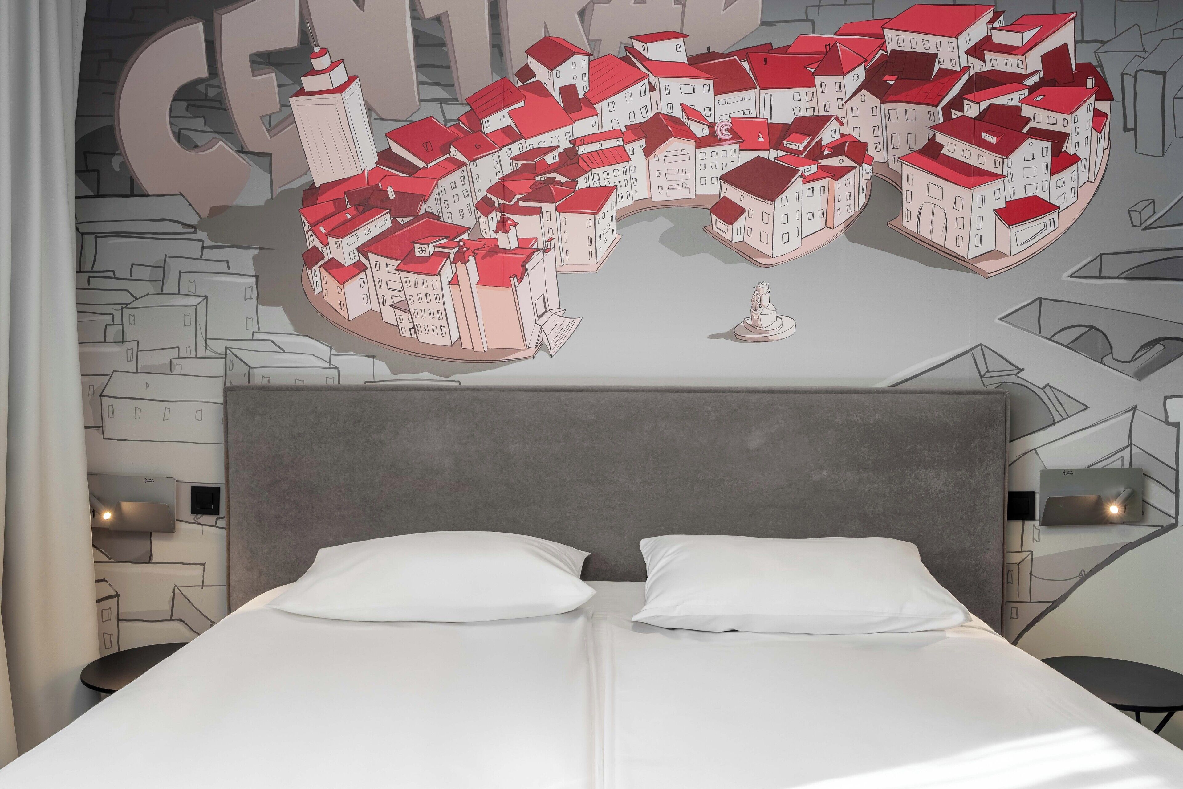 A hotel room with a large bed, two bedside tables, and a wall mural of a cityscape.