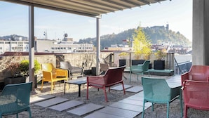 An outdoor seating area with chairs and tables, overlooking a cityscape with buildings and a hill. - ibis Styles Ljubljana Centre (Ljubljana)