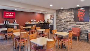 A Red Roof Inn & Suites restaurant with a stone wall, multiple tables and chairs, and a sign indicating free Wi-Fi in all rooms.