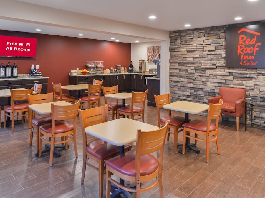 A Red Roof Inn & Suites restaurant with a stone wall, multiple tables and chairs, and a sign indicating free Wi-Fi in all rooms.