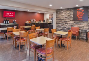 Restaurante de Red Roof Inn & Suites con pared de piedra, varias mesas y sillas, y un letrero que indica Wi-Fi gratis en todas las habitaciones.