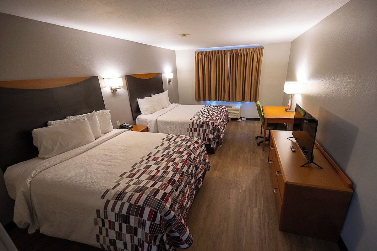 Habitación de hotel con dos camas, un escritorio y una lámpara.