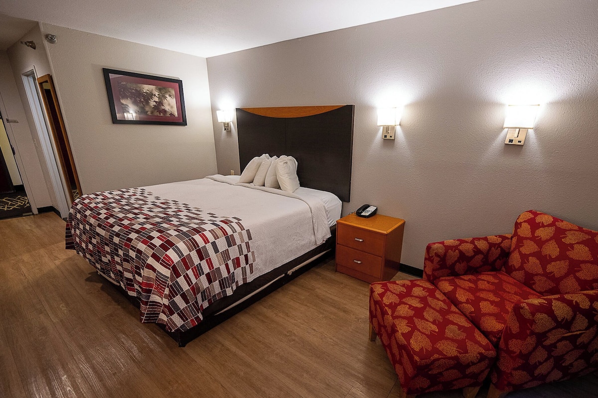 Habitación de hotel con cama, mesita de noche, silla y luces fijadas a la pared.