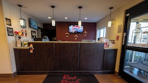 A Red Roof Inn reception desk with a digital clock, a television, and a Red Roof Inn # Suites sign on the floor.
