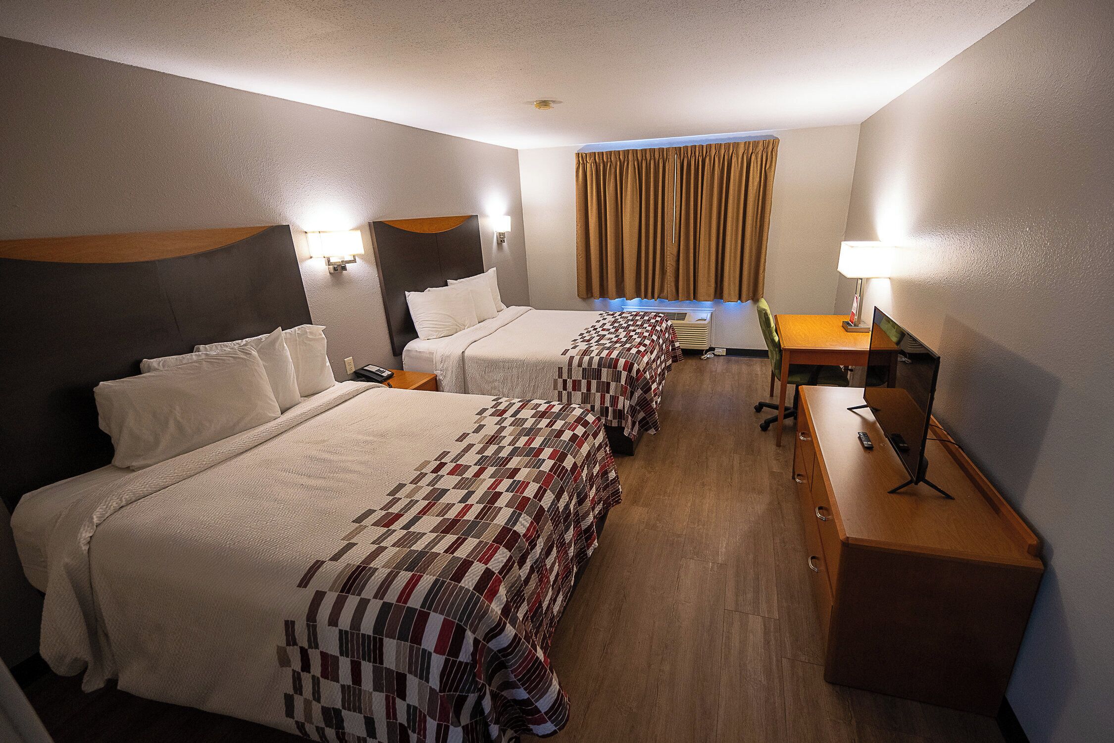 Habitación de hotel con dos camas, un escritorio y una lámpara.