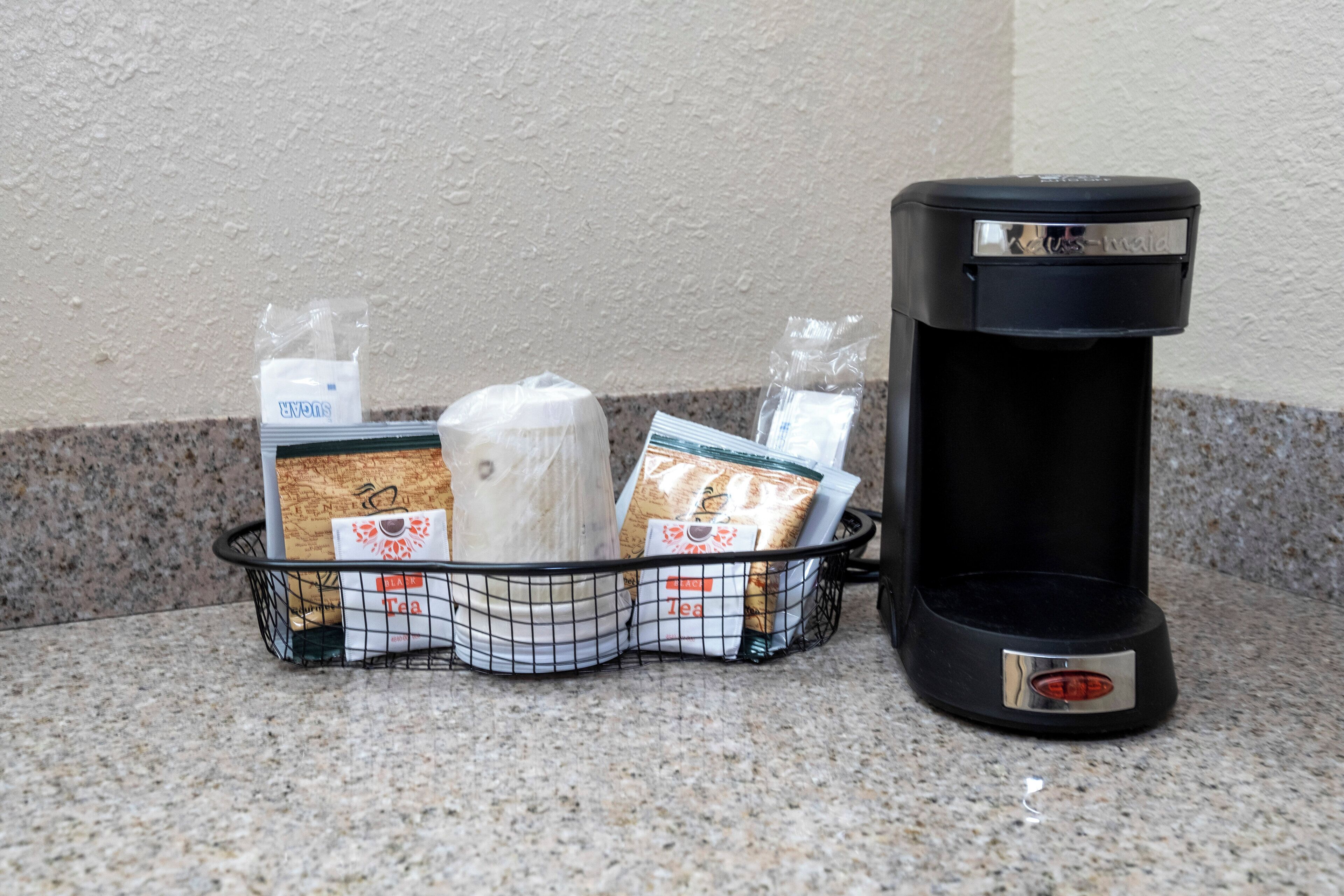 Eine Kaffeemaschine und ein Korb mit Teebeuteln und einer Küchenrolle auf einer Arbeitsfläche.