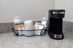 Una cafetera y una cesta con bolsitas de té y un rollo de toallas de papel sobre una encimera.