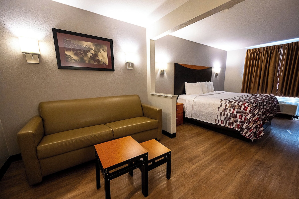 Habitación de hotel con sofá, una mesita, cama con manta estampada y un cuadro en la pared.