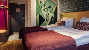 Hotellihuone, jossa on kaksi sänkyä, geometrinen seinätaideteos, kuvioitu pääty ja puulattia.