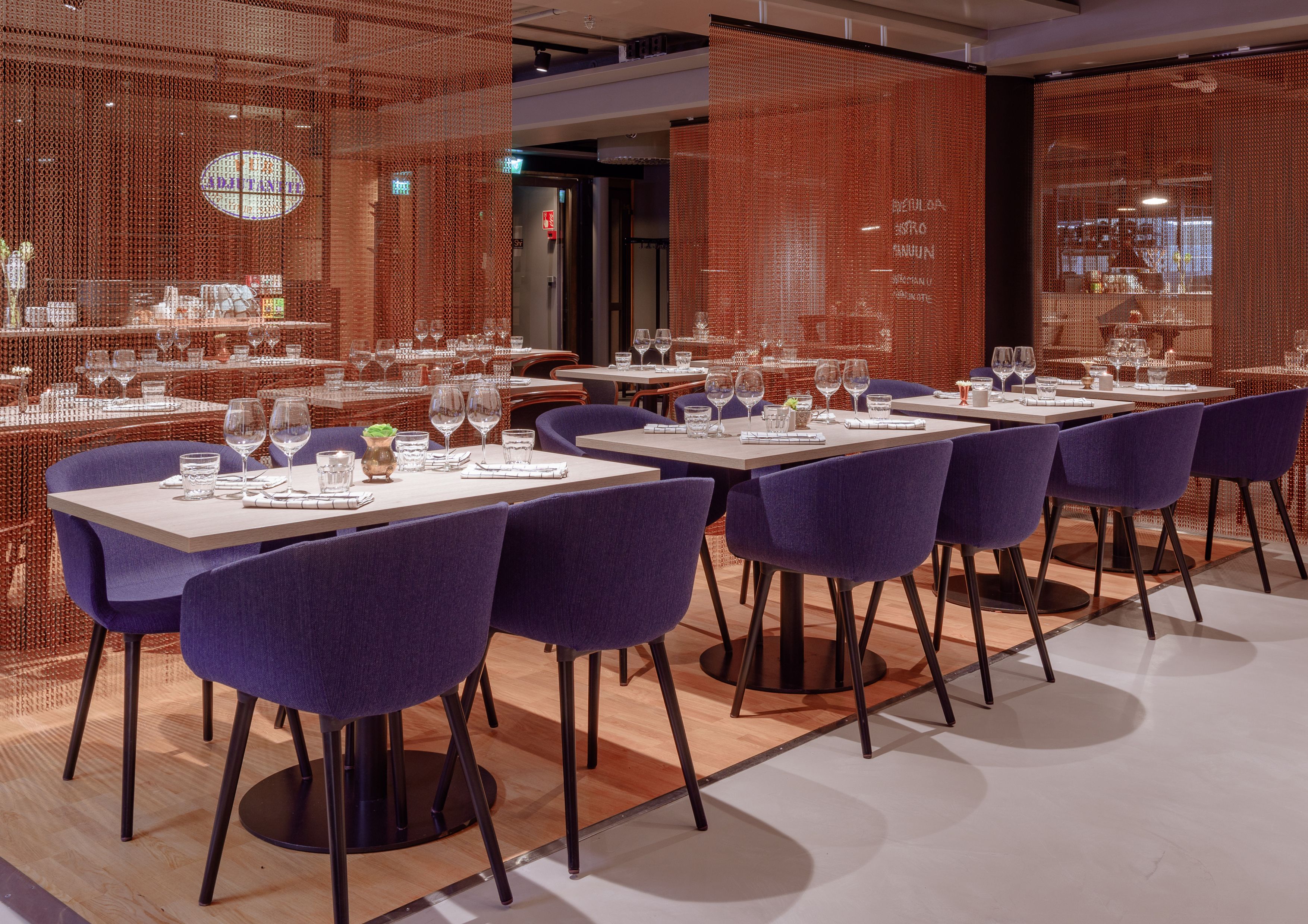 Moderni ravintola, jossa on ruokailuun katetut pöydät, violetit tuolit ja taustalla tiiliseinä.