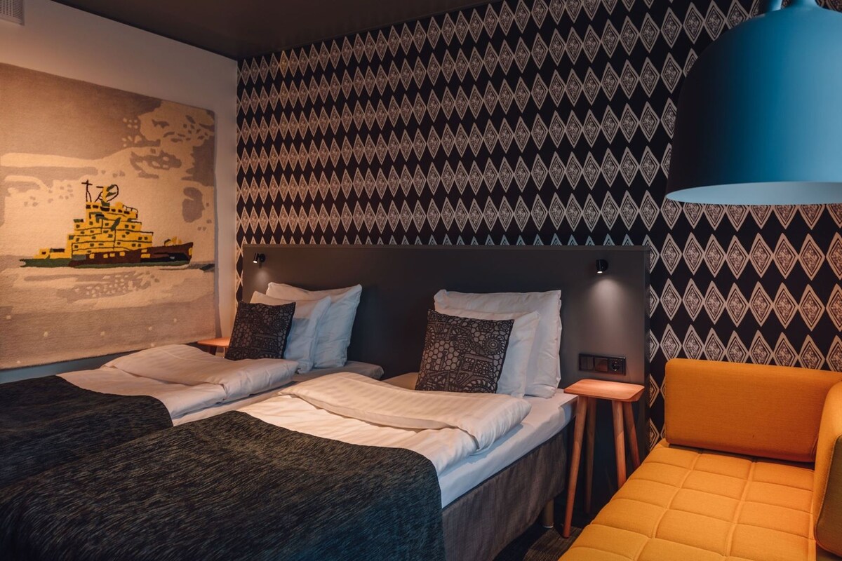 A hotel room with a bed, a sofa, a patterned wall, and a large blue lamp.