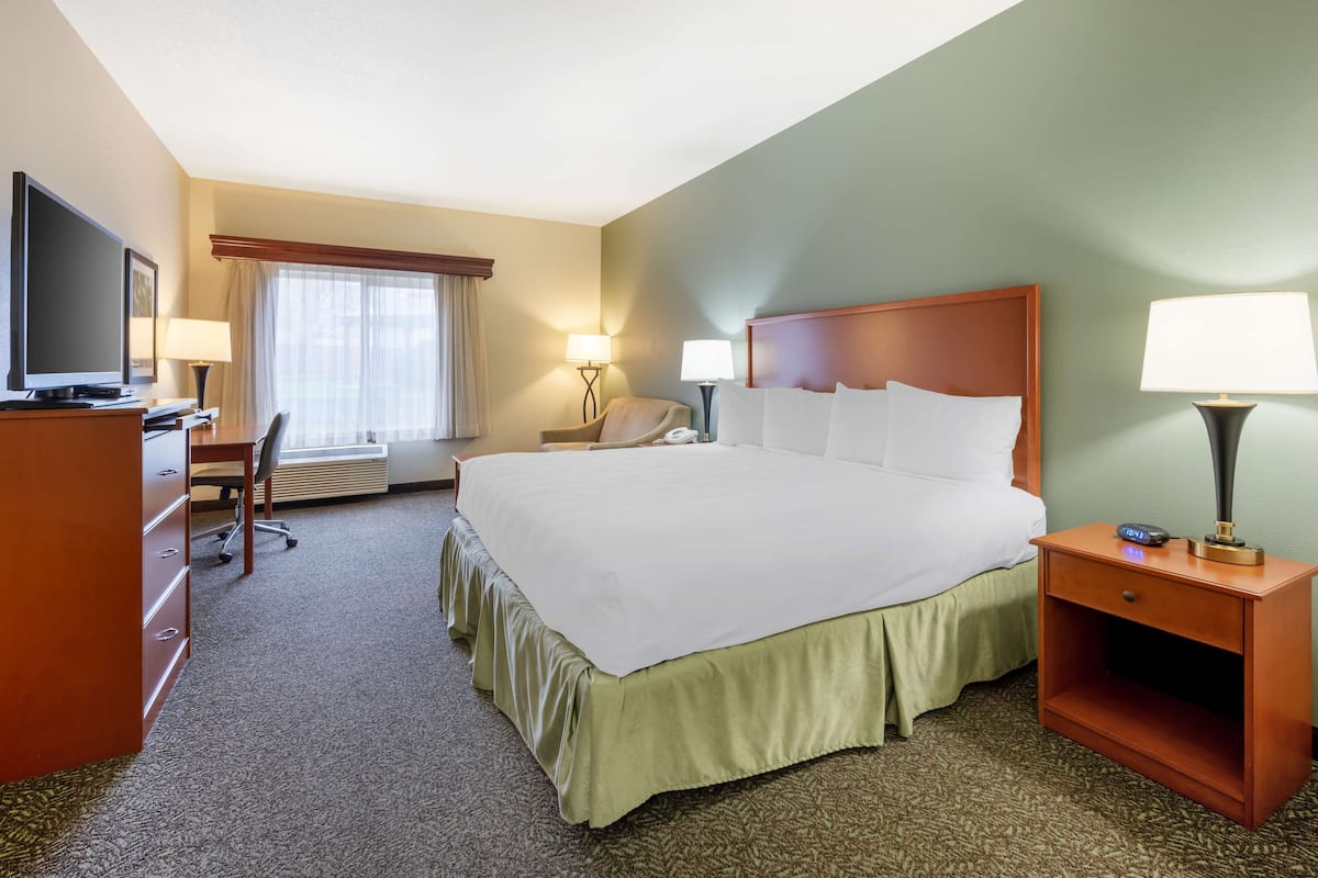 A hotel room with a large bed, a desk with a television, a chair, two bedside lamps, and a window with curtains.