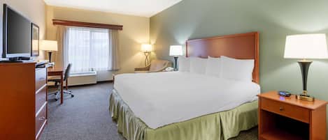 A hotel room with a large bed, a desk with a television, a chair, two bedside lamps, and a window with curtains.