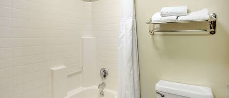 A bathroom with a bathtub, a shower curtain, a toilet, and a towel rack with towels.