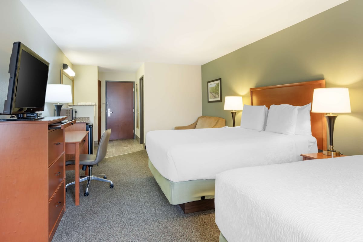 A hotel room with a desk, two beds, a chair, and a television.