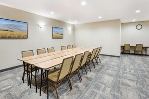 Un salón de conferencias con una larga mesa y sillas, un reloj en la pared y dos cuadros enmarcados.
