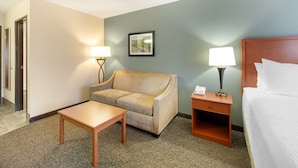 Una habitación de hotel con cama, sofá, mesa, dos lámparas y un cuadro en la pared.