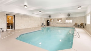 Una piscina interior con agua cristalina, una escalera y algunas sillas alrededor de la zona de la piscina.