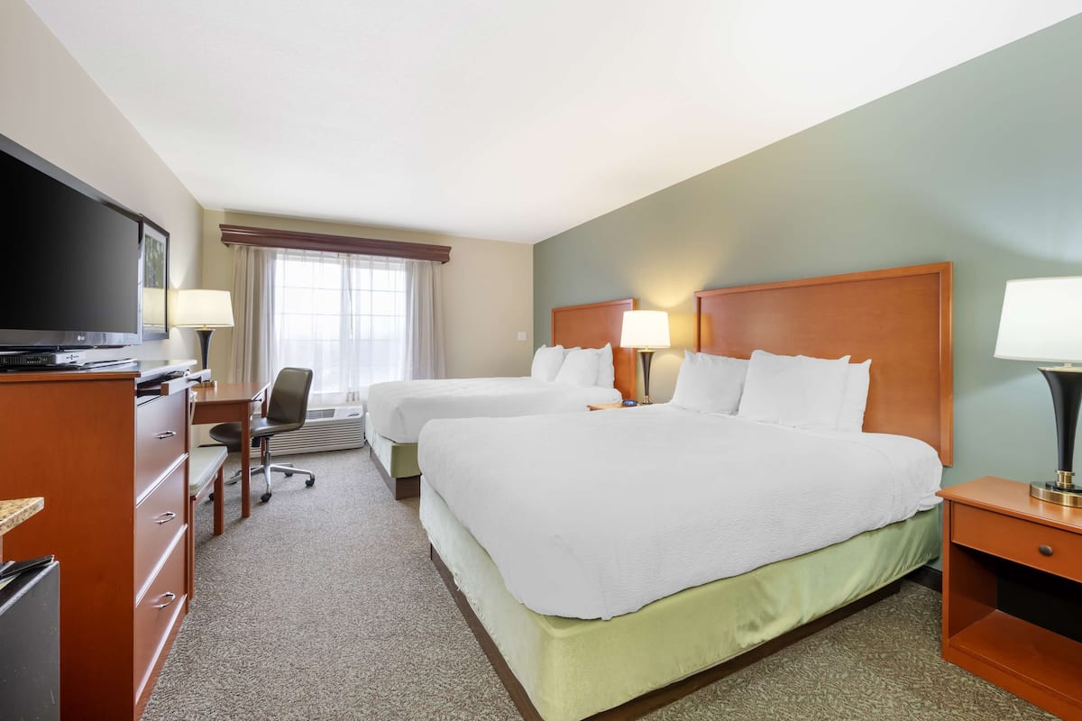 A hotel room with two beds, a desk, a television, and a window with curtains.