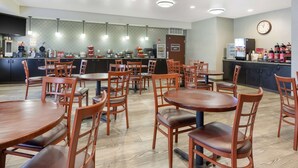 Un restaurante moderno con varias mesas y sillas, una zona de cocina con una máquina de café y un reloj en la pared.