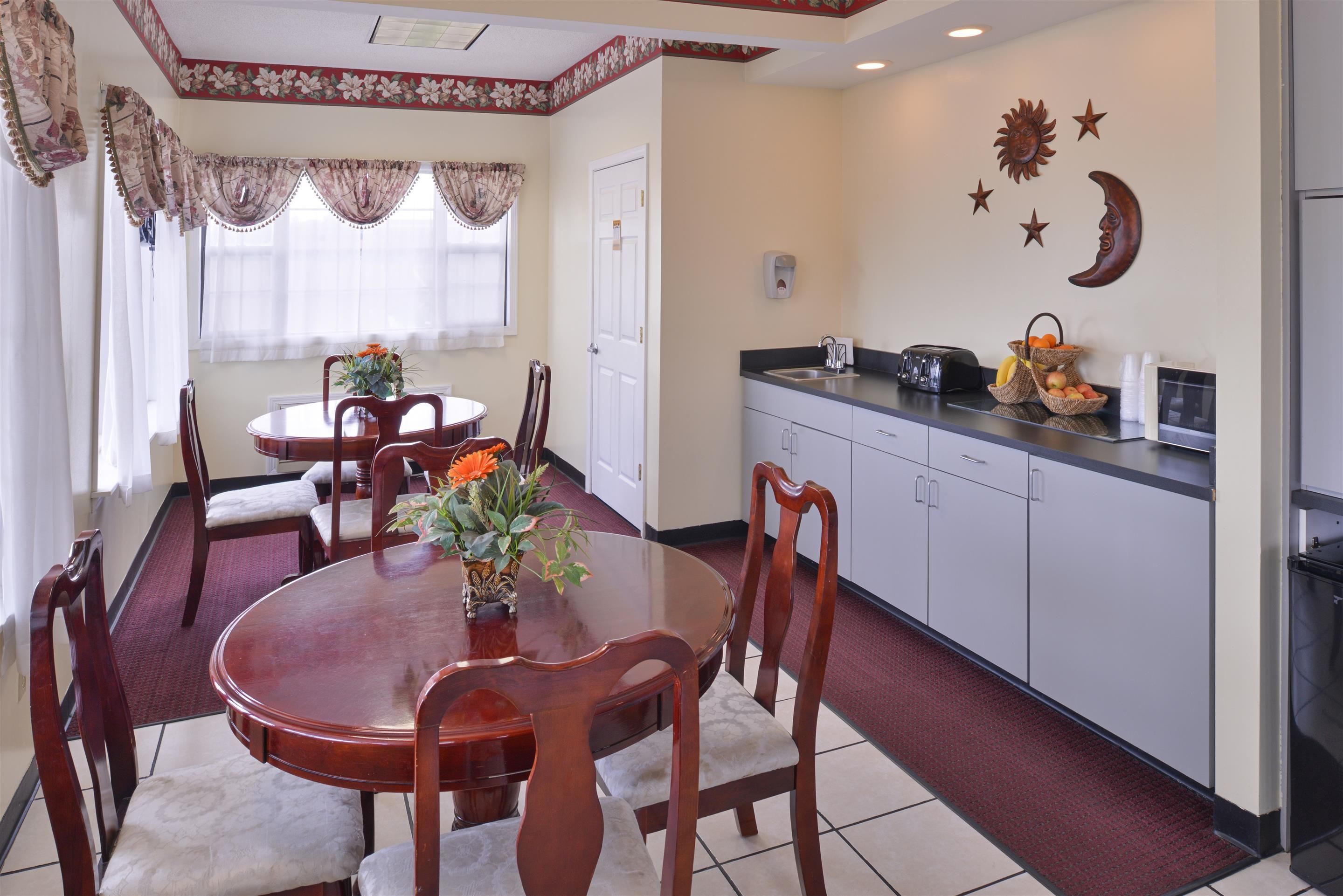 A dining area with a round table, chairs, and a vase of flowers. There is a kitchen area with cabinets and a countertop.
