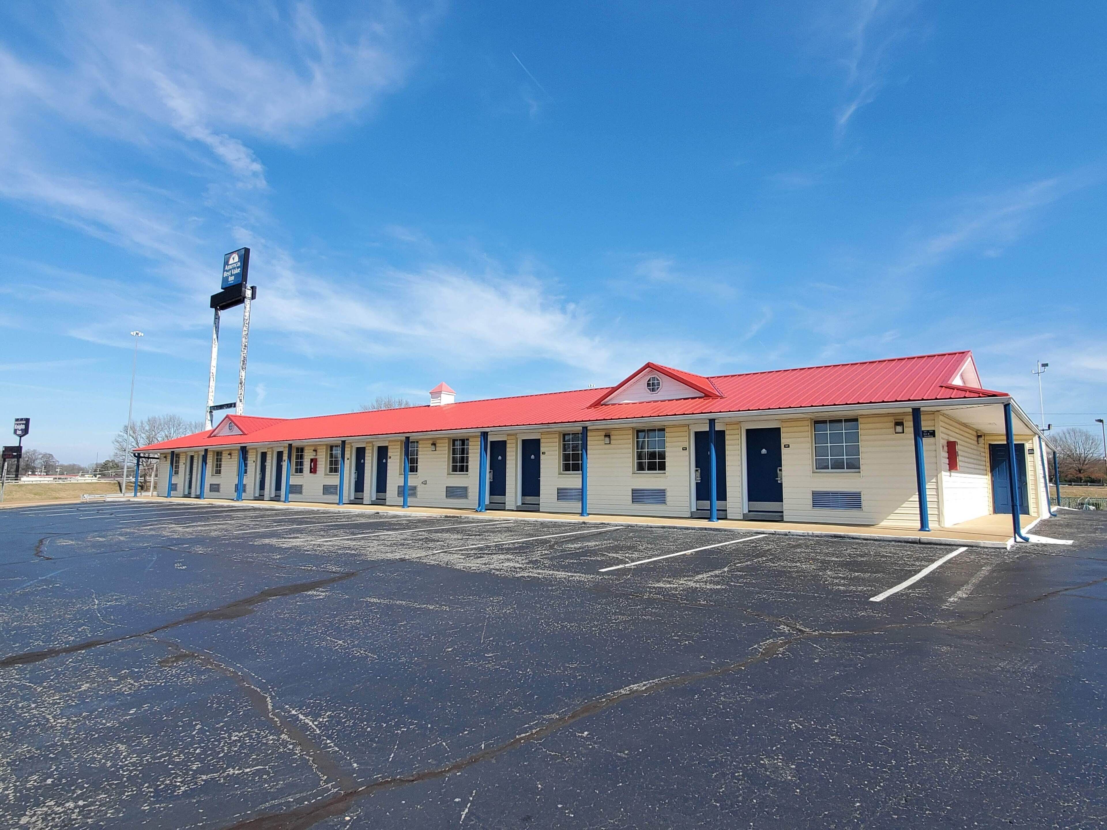 A motel with a red roof and blue accents, featuring a large parking lot in front.