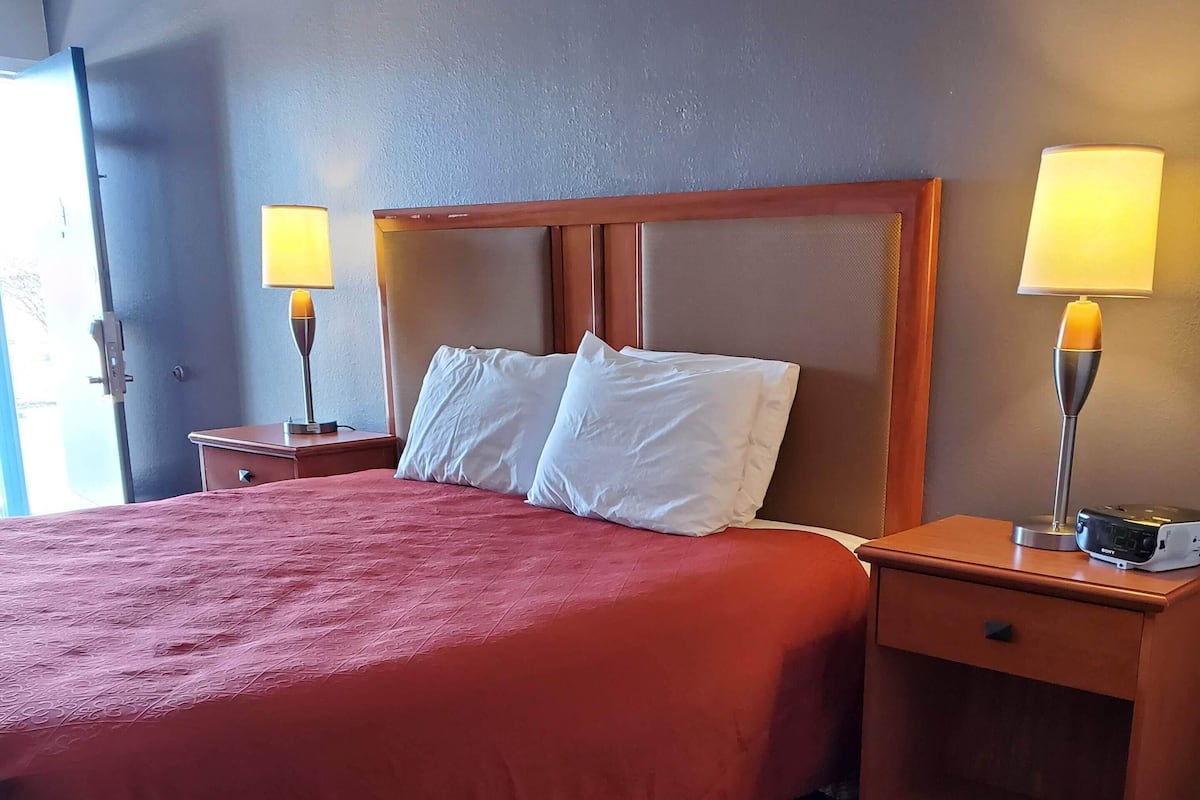 Et hotelværelse med en stor seng, to sengeborde med lamper, et træ-natbord og en lille skammel.