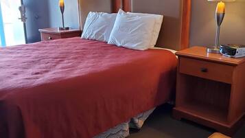 A hotel room with a large bed, two bedside tables with lamps, a wooden nightstand, and a small ottoman.