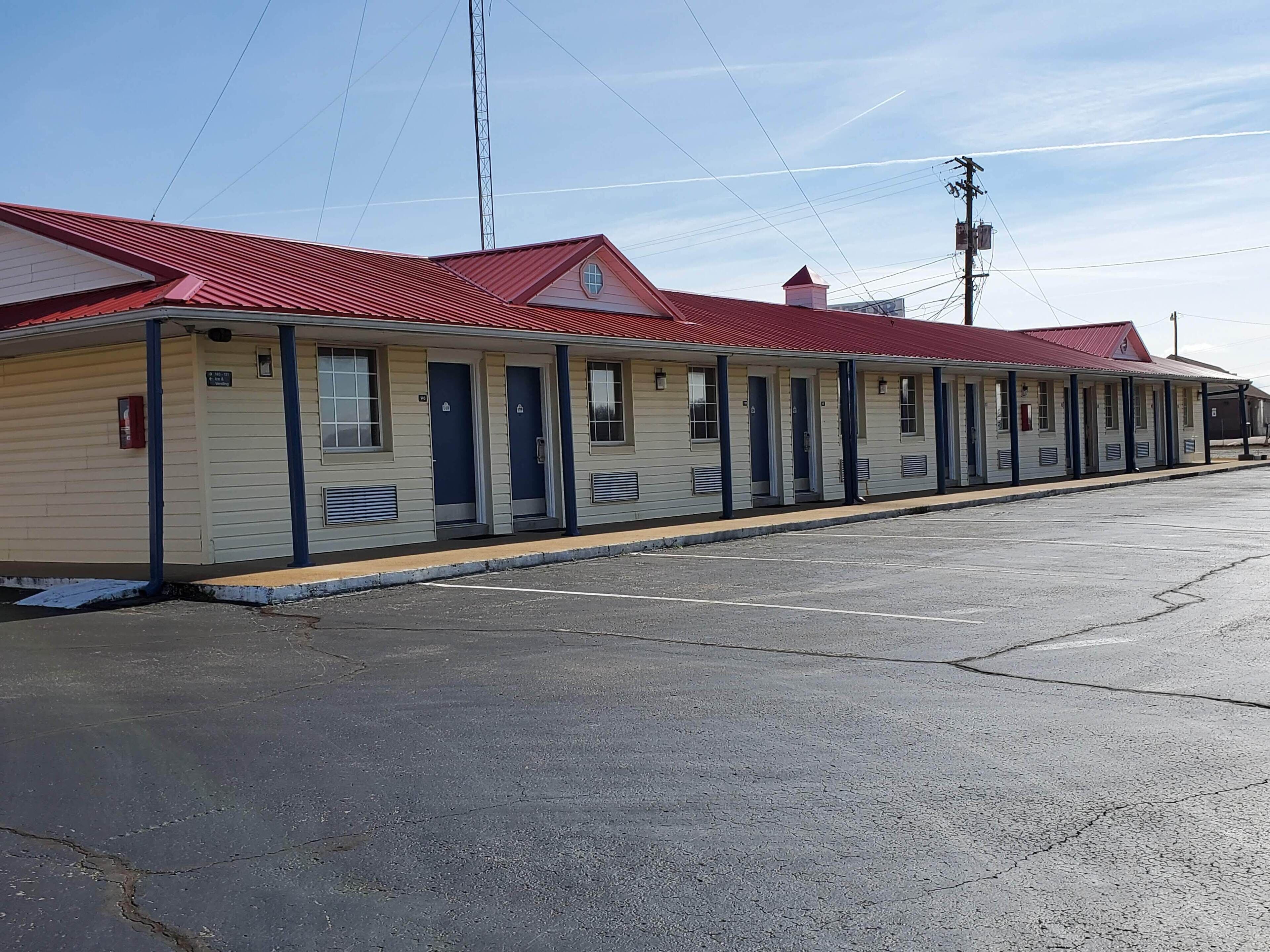 Een rij motelgebouwen met één verdieping, met een rood dak, beige gevelbekleding en een parkeerplaats ervoor.