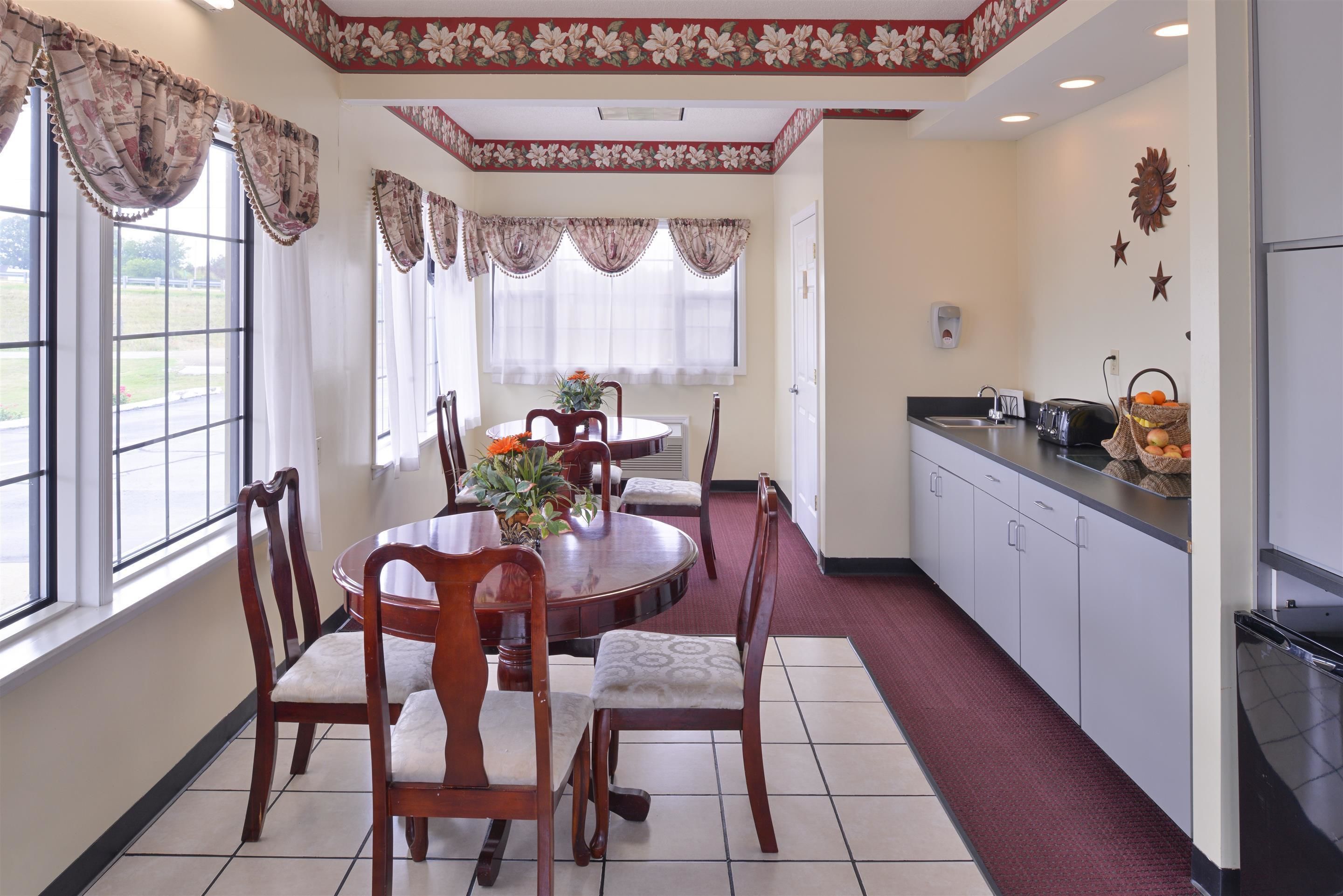 A dining area with a round table and chairs, a kitchen with cabinets and a countertop, and large windows with curtains.