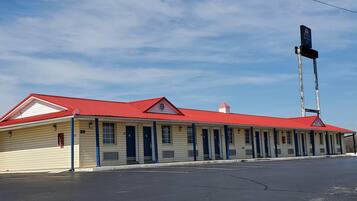A two-story motel with a red roof and beige siding, featuring a row of single rooms with dark blue doors.