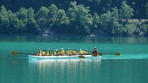 Un equipo de remo en un bote sobre un lago tranquilo, con árboles densos al fondo.